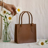 Walnut brown bag next to vase of daisys