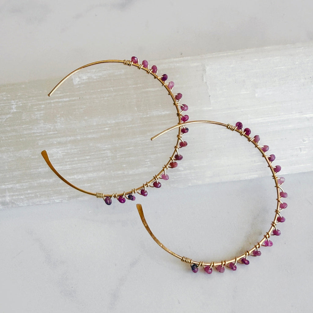 Gold hoop earrings with pink gemstones on a light background
