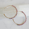 Gold hoop earrings with pink gemstones on a light background