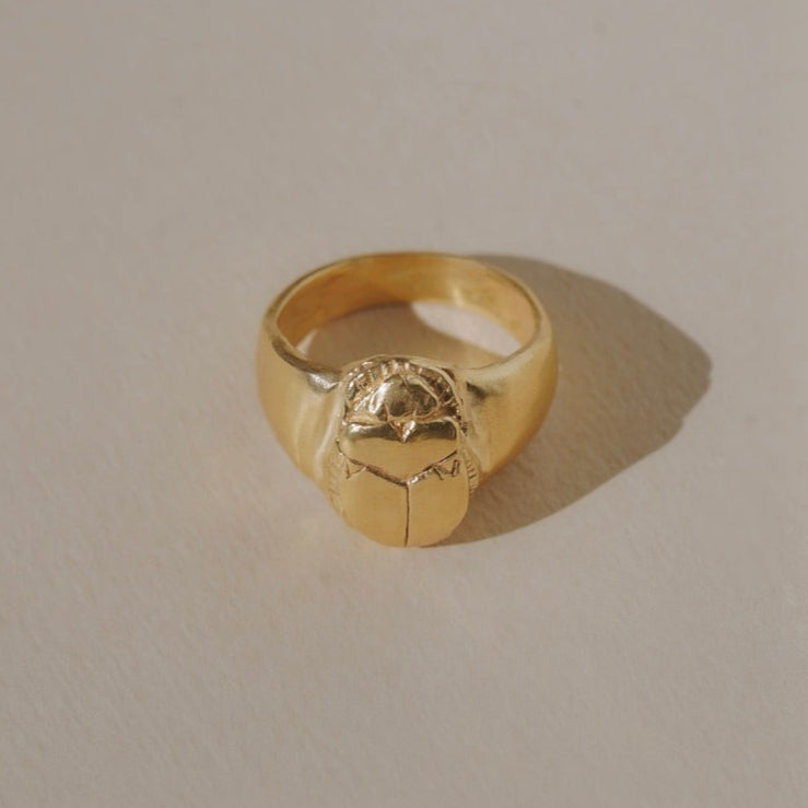 Gold ring with a scarab beetle design on a beige background