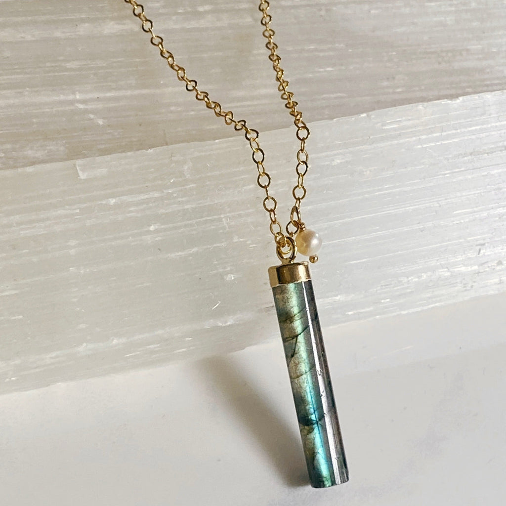Necklace with a cylindrical pendant on a light stone background