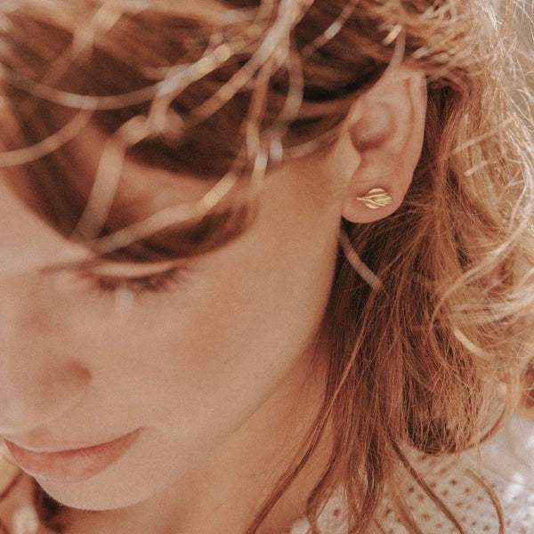 Close-up of a person wearing gold earrings with a blurred background