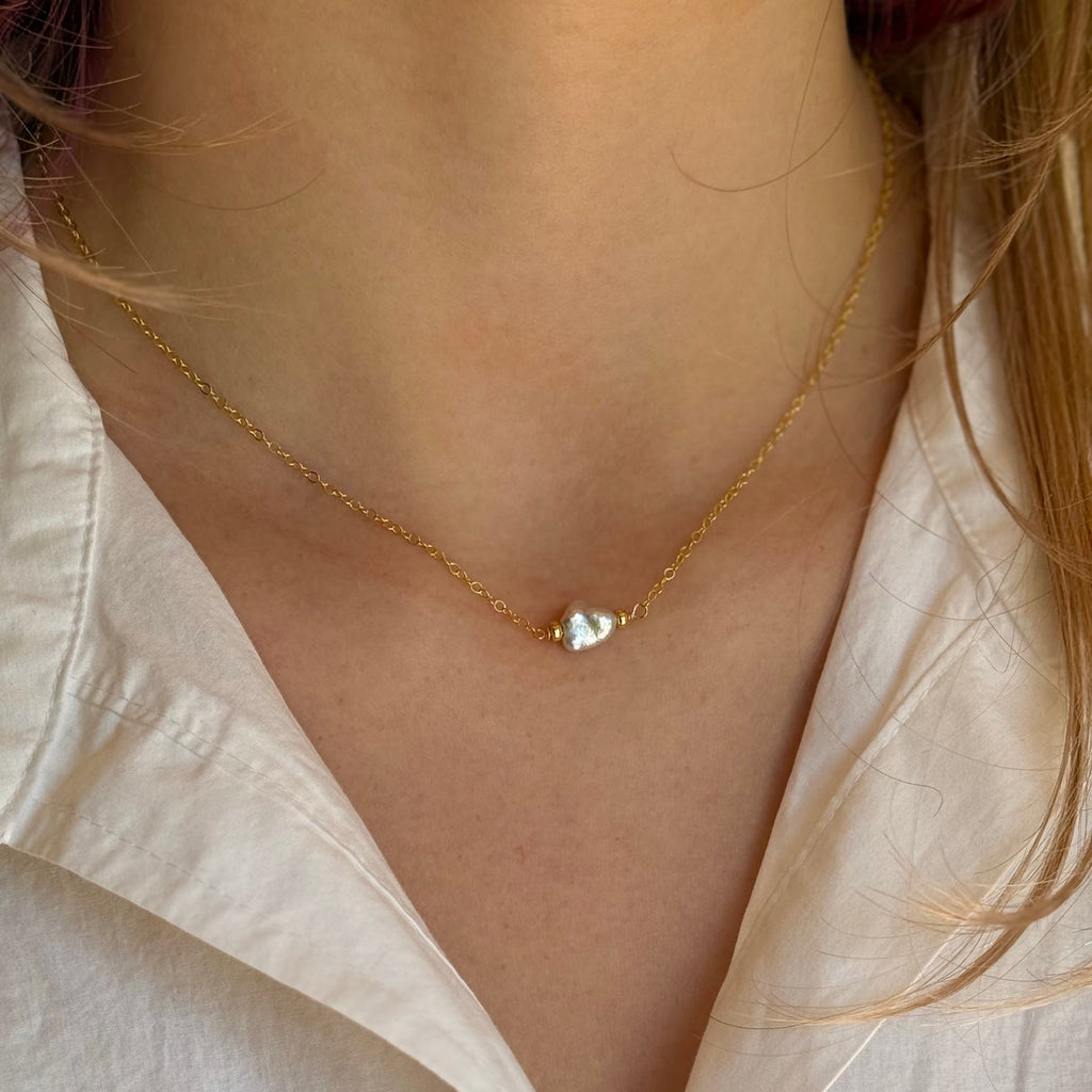 Gold necklace with a small pearl worn by a person in a light-colored shirt.
