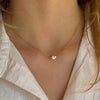 Gold necklace with a small pearl worn by a person in a light-colored shirt.