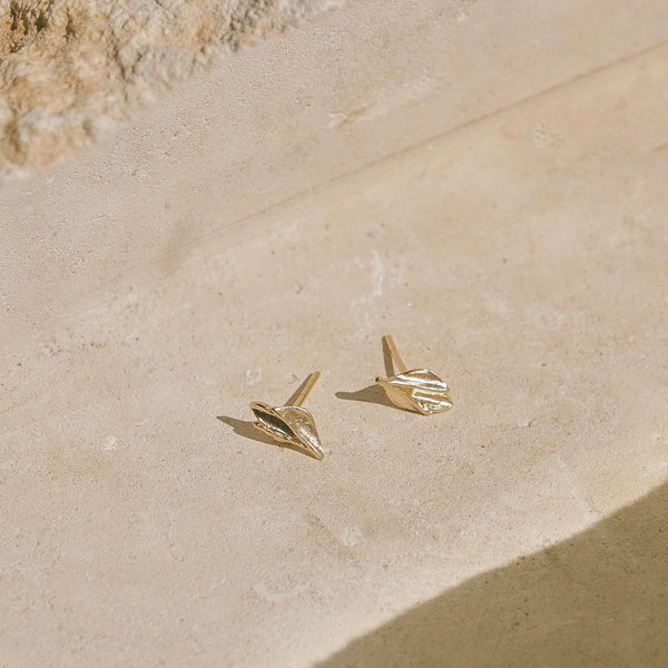 Gold bud-shaped earrings on a beige stone surface