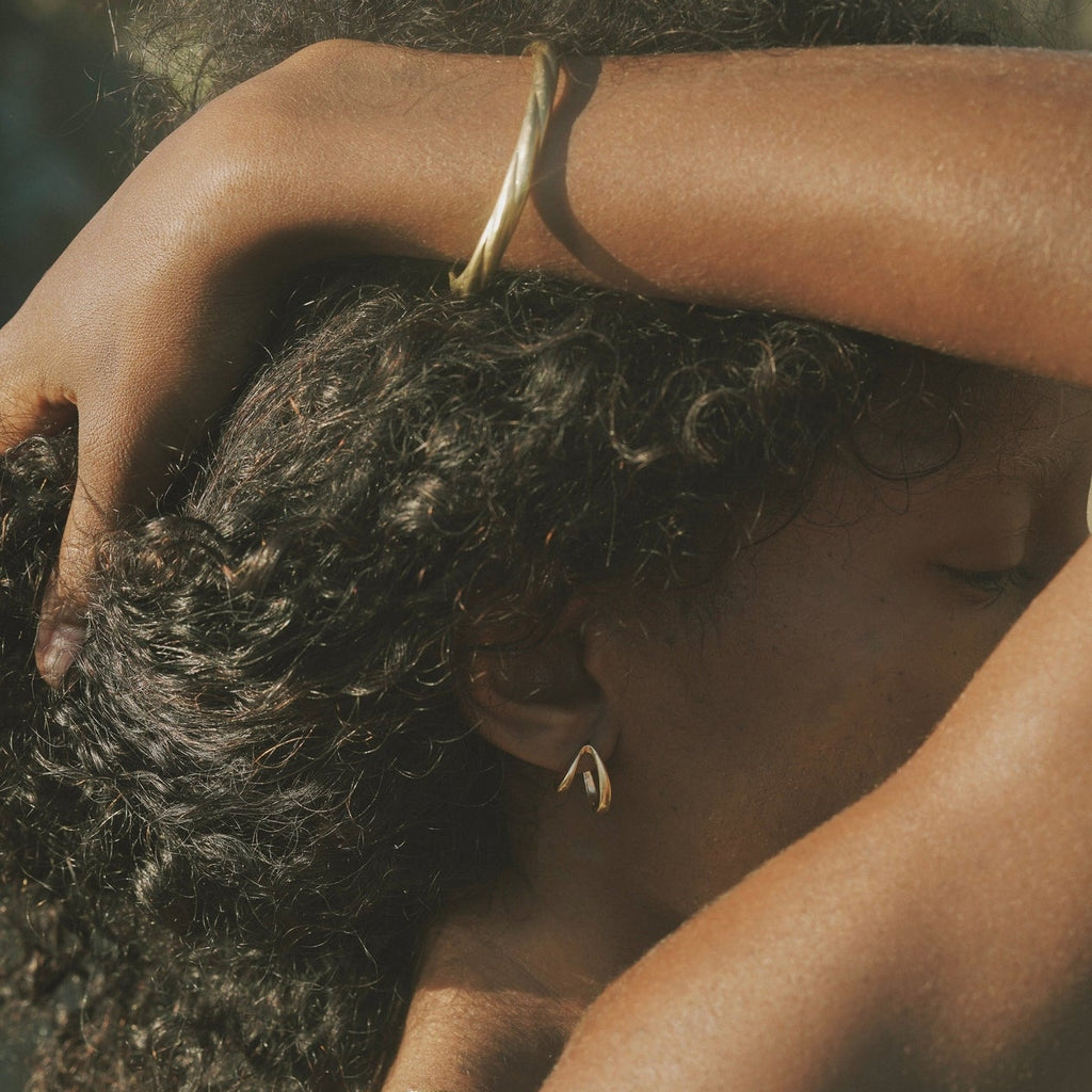Close-up of a person with textured hair and a gold bracelet, with a blurred natural background.