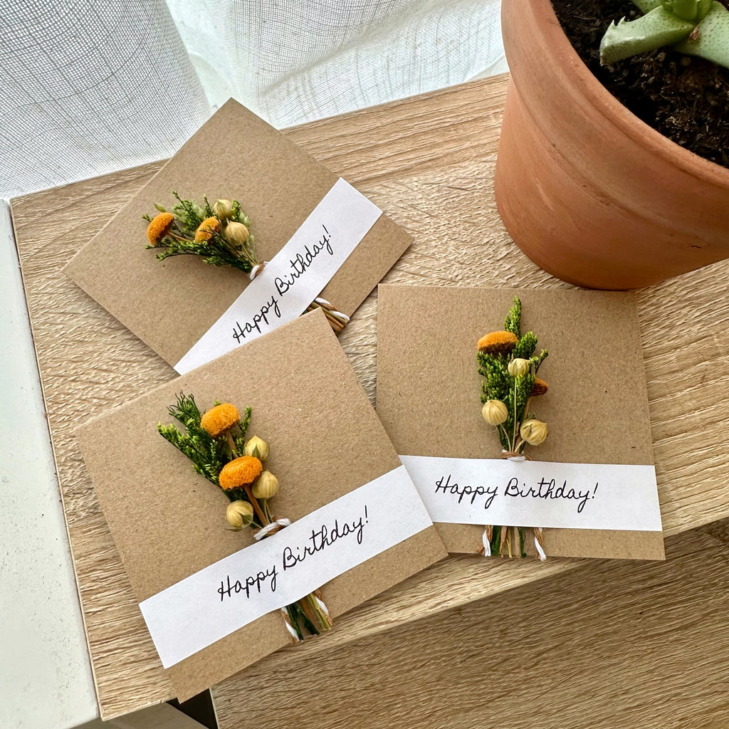 Three handmade birthday cards with floral arrangements on a wooden surface.
