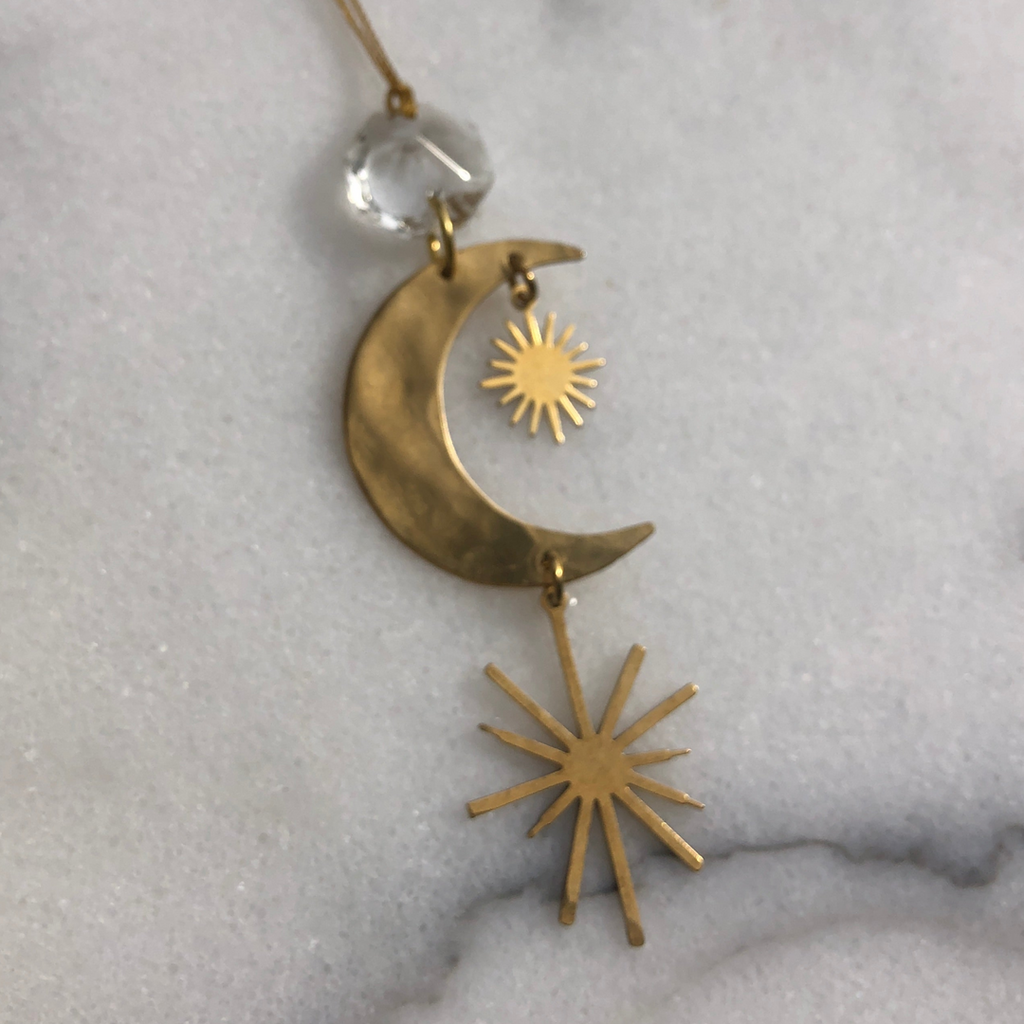 Gold pendant with moon and sun design on a textured gray background