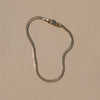 A gold-toned snake chain necklace with a lobster clasp, displayed on a solid beige background.
