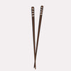 A pair of blackened wooden chopsticks with a flame pattern, standing upright against a white background.